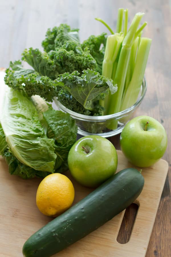 Ingredients for Green Juice on table: kale, celery, green apples, lemon, cucumbers, romaine lettuce