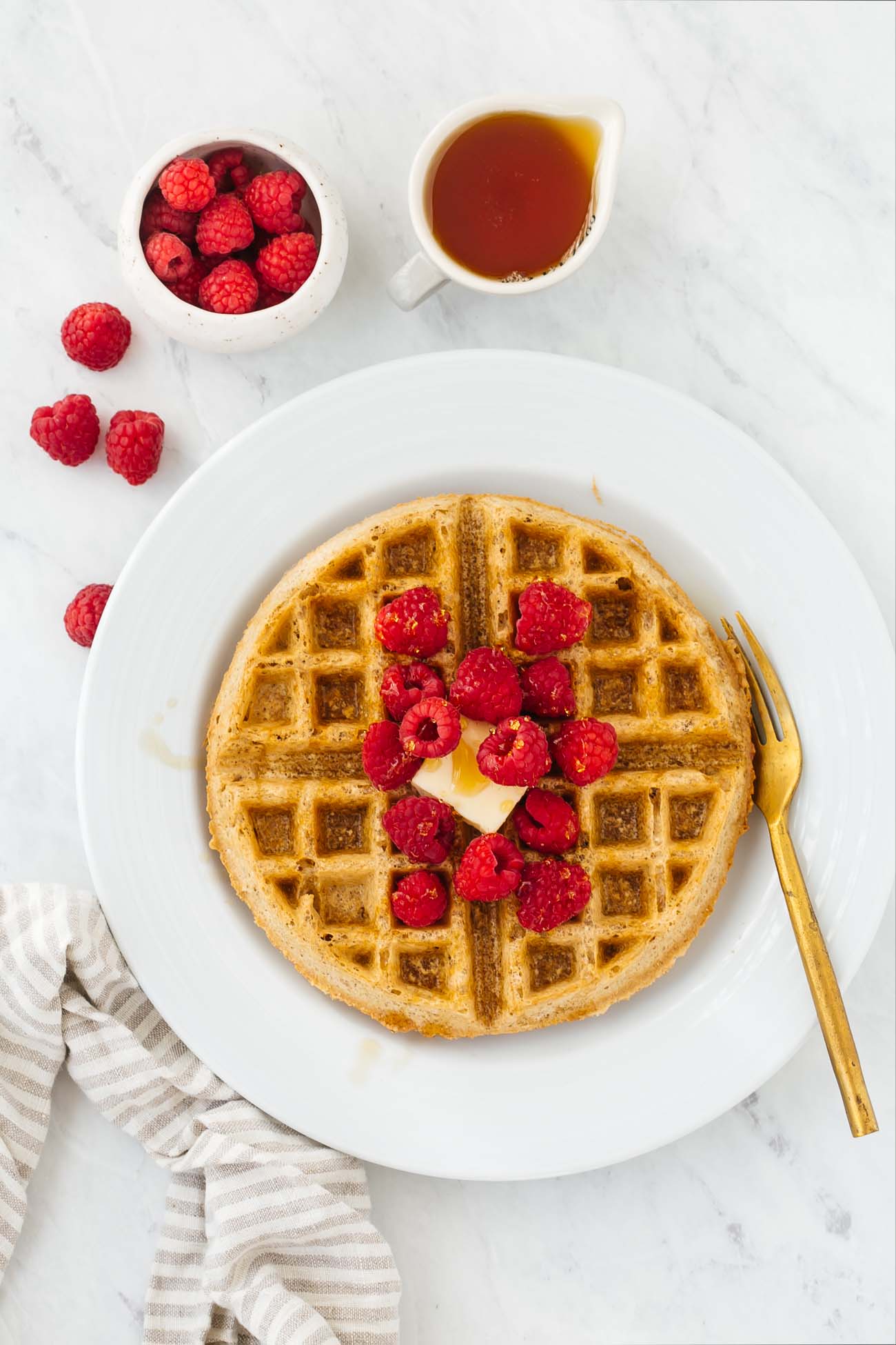 Overhead view of a gluten-free peanut butter waffle topped with fresh raspberries.