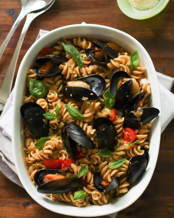 White baking dish with Whole Wheat Fusilli with Mussels and cherry tomatoes inside with basil on top
