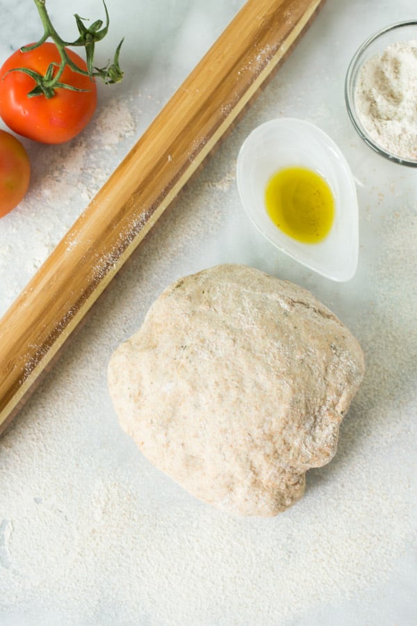 whole wheat pizza dough beside a rolling pin and oil