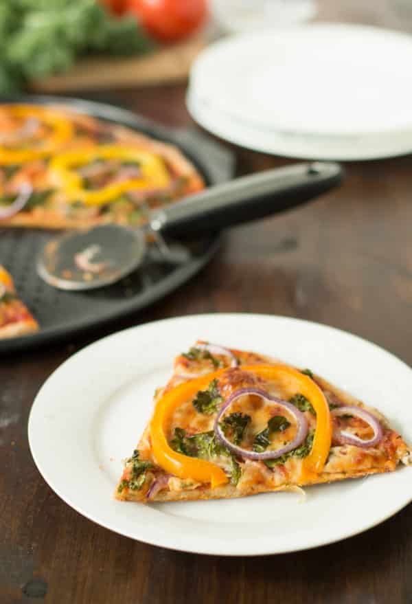 Slice of Kale, Peppers, Red Onion Pizza on a while plate