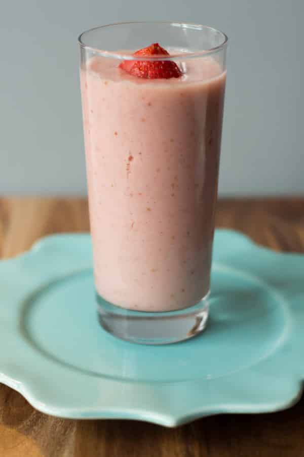 Strawberry and papaya smoothie in a glass cup on a teal plate