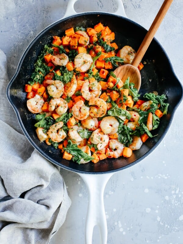 overhead view of a white skillet containing shrimp, sweet potato and kale