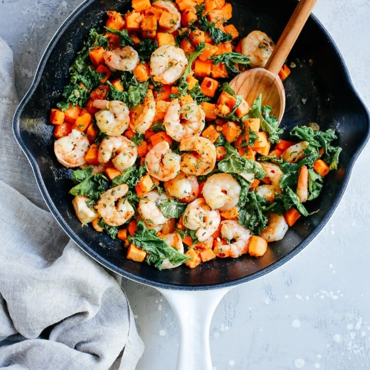 overhead view of a white skillet containing shrimp, sweet potato and kale