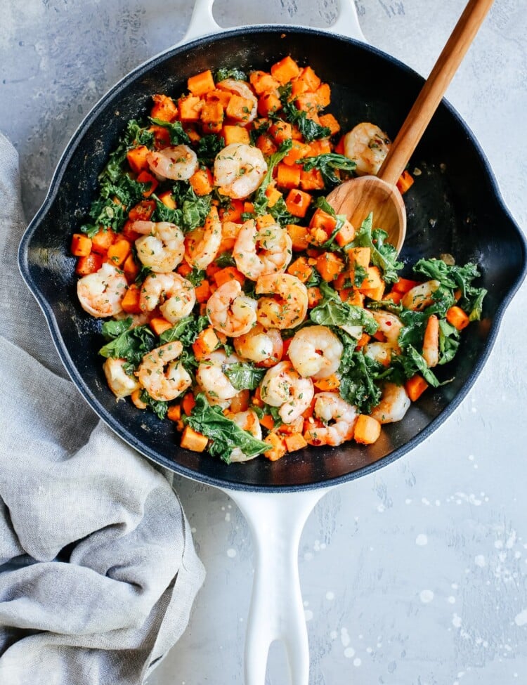 overhead view of a white skillet containing shrimp, sweet potato and kale