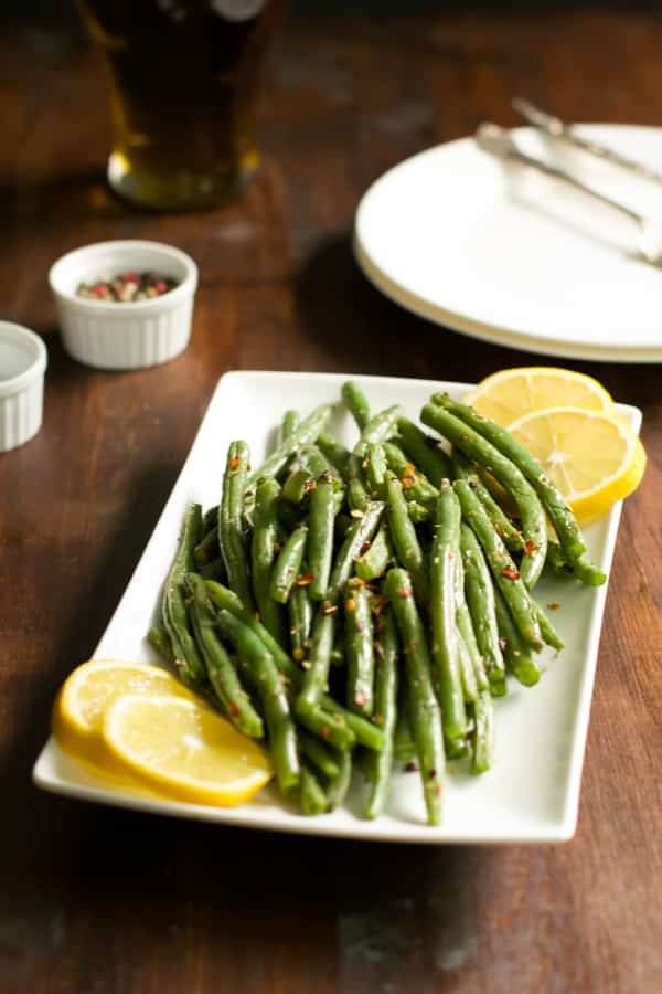A white serving plate of crispy green beans with lemon slices around it.