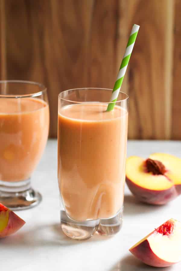 Peach Carrot Smoothie in a tall glass with a green straw.