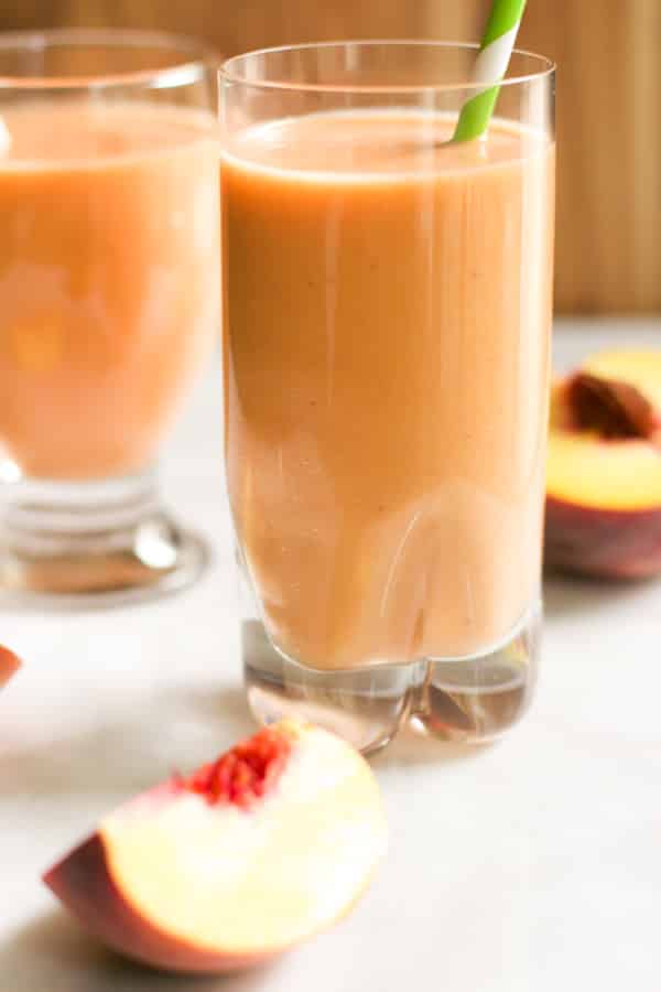 Peach Carrot Smoothie in a glass with peaches scattered.