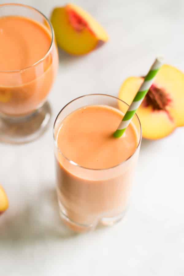 Peach Carrot Smoothie in a glass with peaches in the background. 