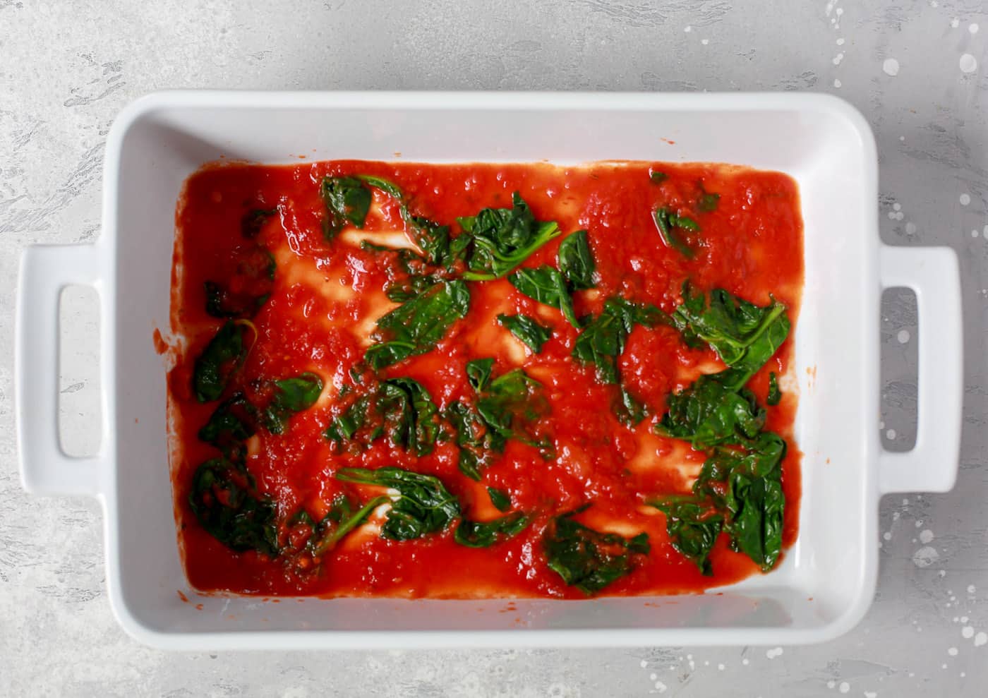 overhead view of a white casserole containing tomato sauce and spinach