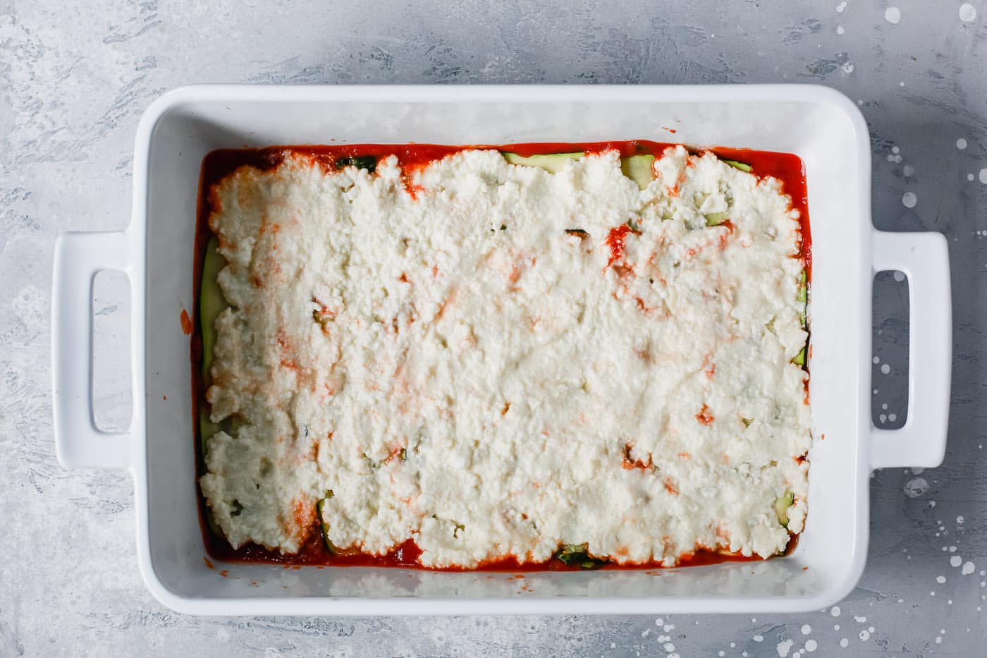 overhead view of a white casserole containing tomato sauce, zucchini noodles and ricotta 