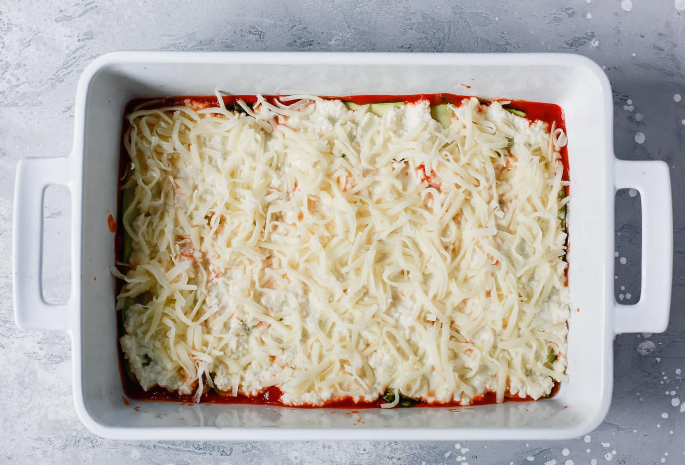 overhead view of a white casserole containing tomato sauce, zucchini noodles and mozzarella cheese