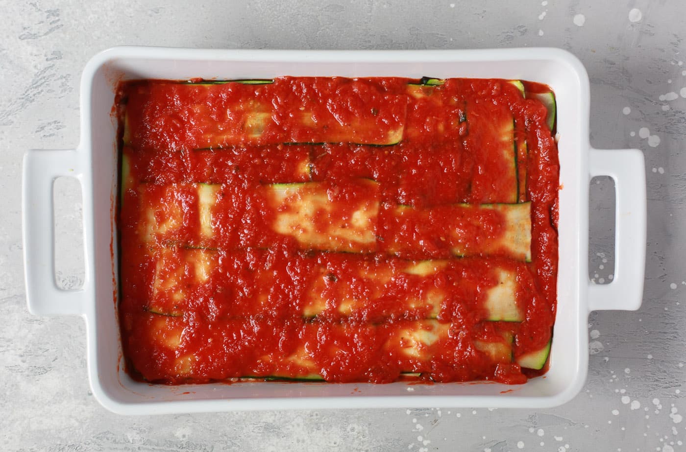 overhead view of a white casserole containing zucchini noodles and tomato sauce