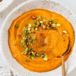 Close up of a bowl of carrot leek soup with green onions as garnish.