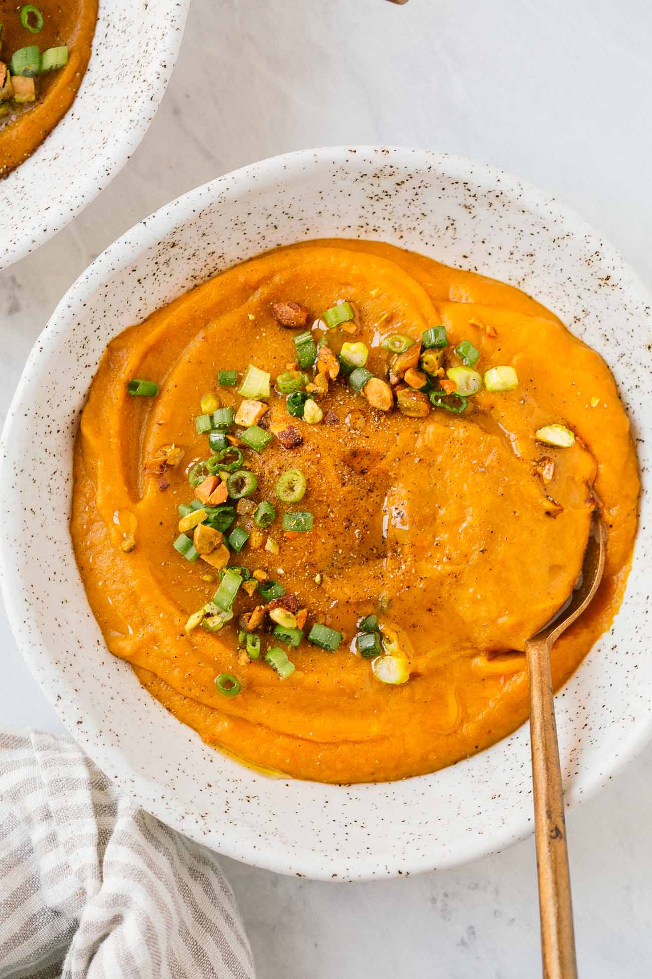 Close up of a bowl of carrot leek soup with green onions as garnish.