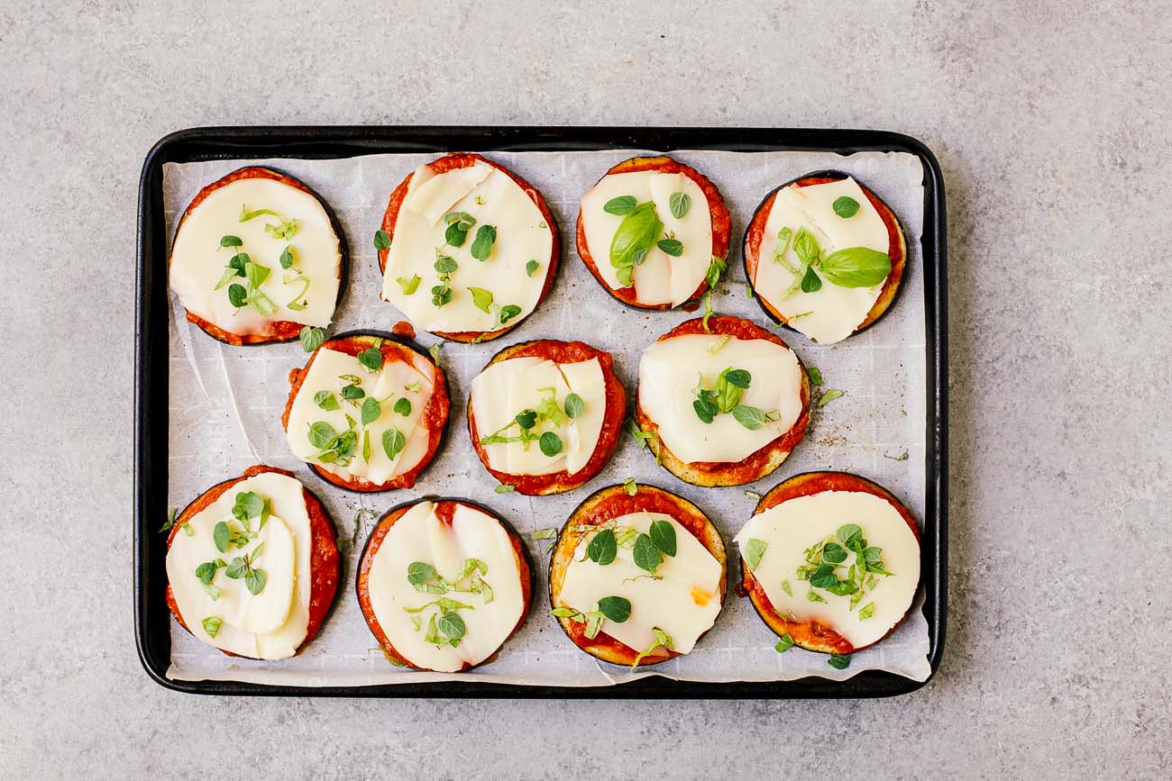 raw slices of eggplant with tomato sauce on top and mozzarella on a baking sheet