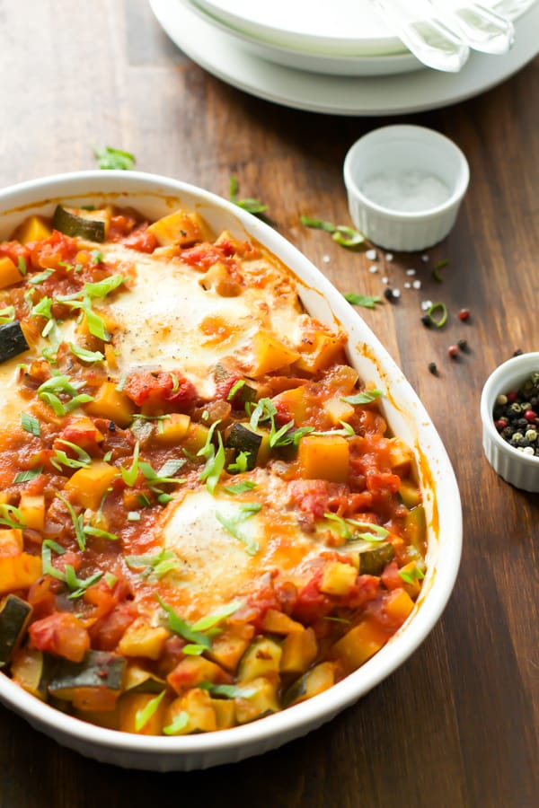 A white baking dish with baked eggs and vegetables.