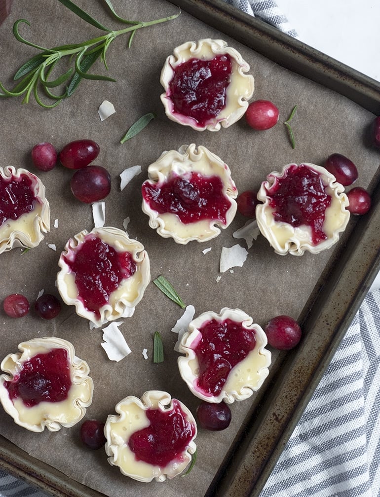 Multiple cranberry brie tarlets on a sheet pan.