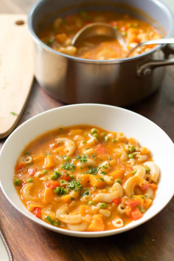 overhead view of a bowl containing pasta soup with sweet potato and peas