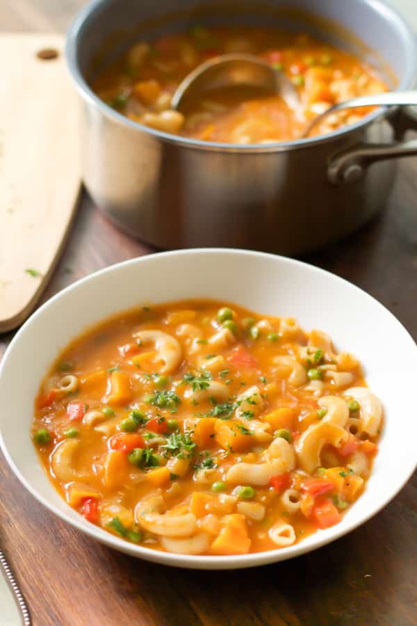 overhead view of a bowl containing pasta soup with sweet potato and peas