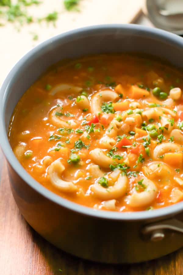 A bowl of pasta soup with sweet potato and peas.