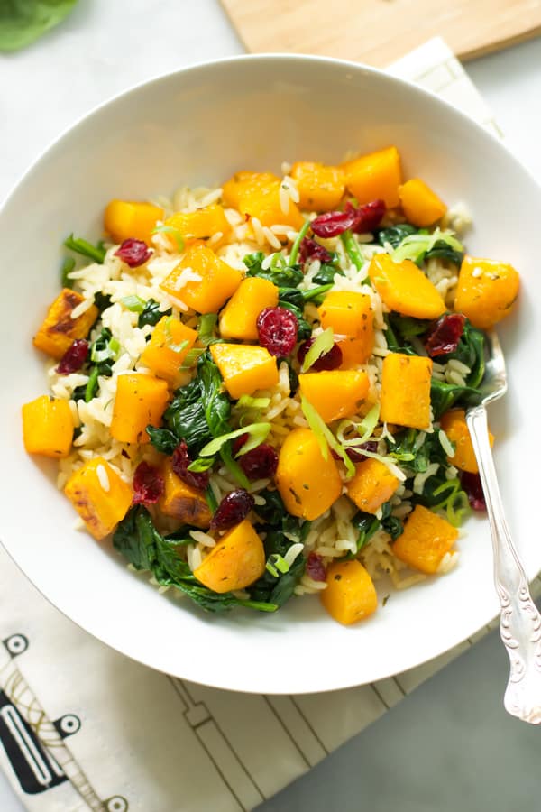 A white bowl of rice with roasted butternut squash and dried cranberries with a fork inside.