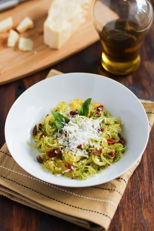 An overhead image of a white bowl of spaghetti squash with sun-dried tomatoes and basil.