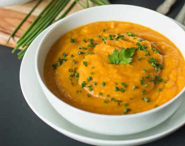 A bowl of spicy carrot soup with garnish on top and in the background.