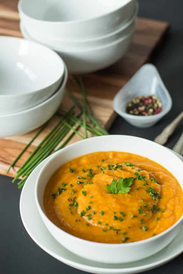 An angled photo of a bowl of carrot parsnip soup with a stack of empty bowls behind it.