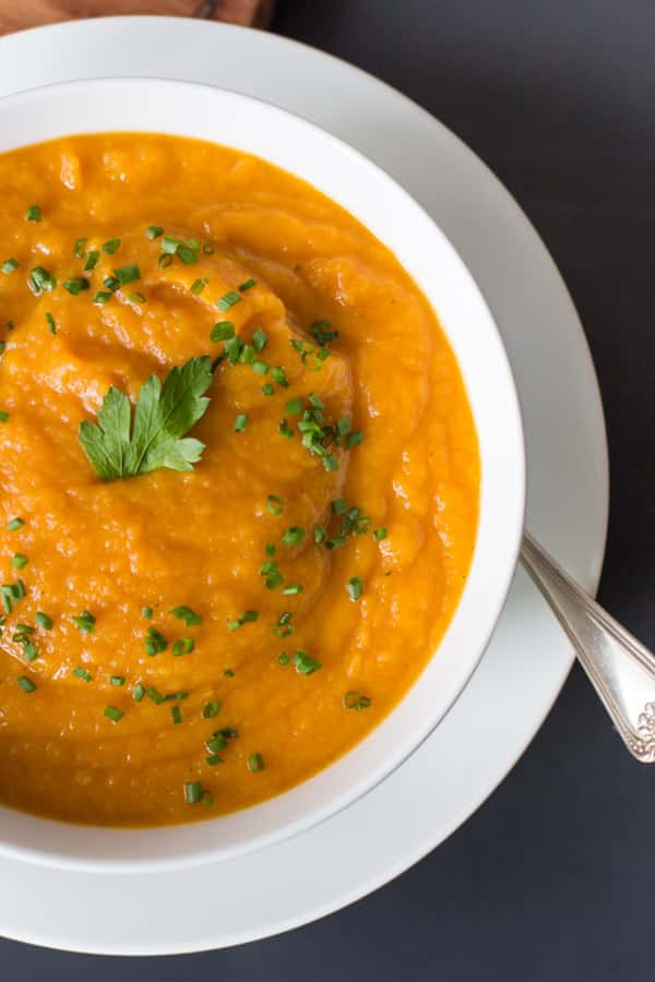 An overhead image of a close up of a white bowl of carrot parsnip soup.