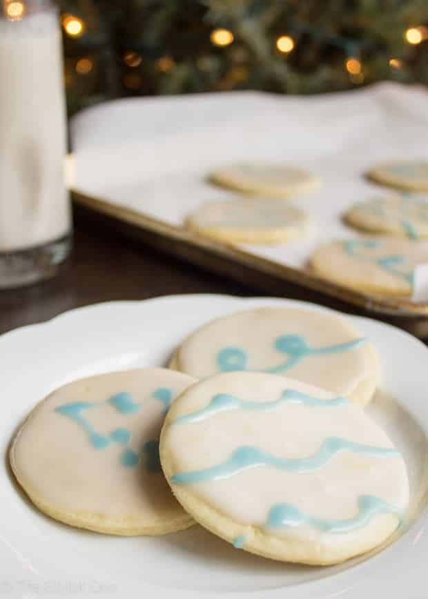 Three Christmas sugar cookies with white and blue icing on a plate.