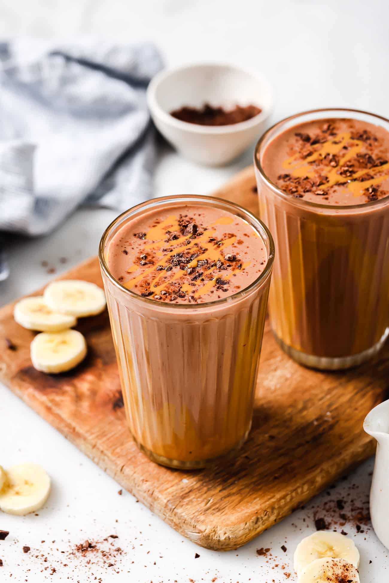Two peanut butter chocolate smoothies on a wooden cutting board.