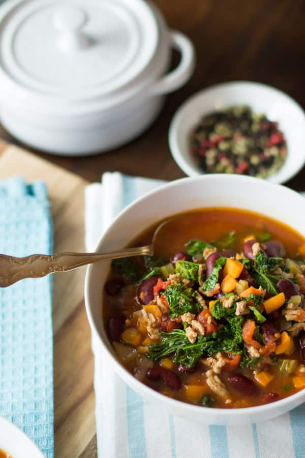 A white bowl with extra-lean turkey chill with kale inside with a spoon placed in.