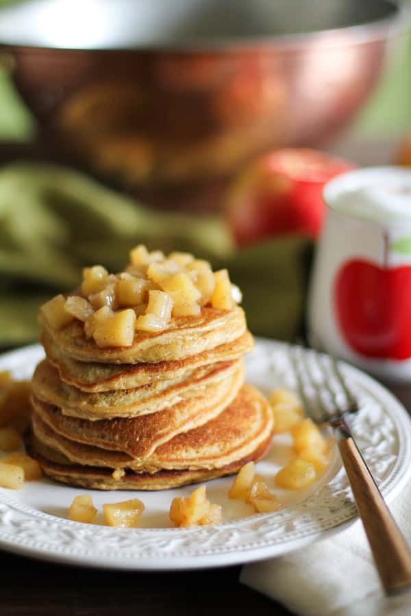 Apple-Cinnamon-Pancakes A small stack of apple cinnamon pancakes topped with stewed apples on a white plate.