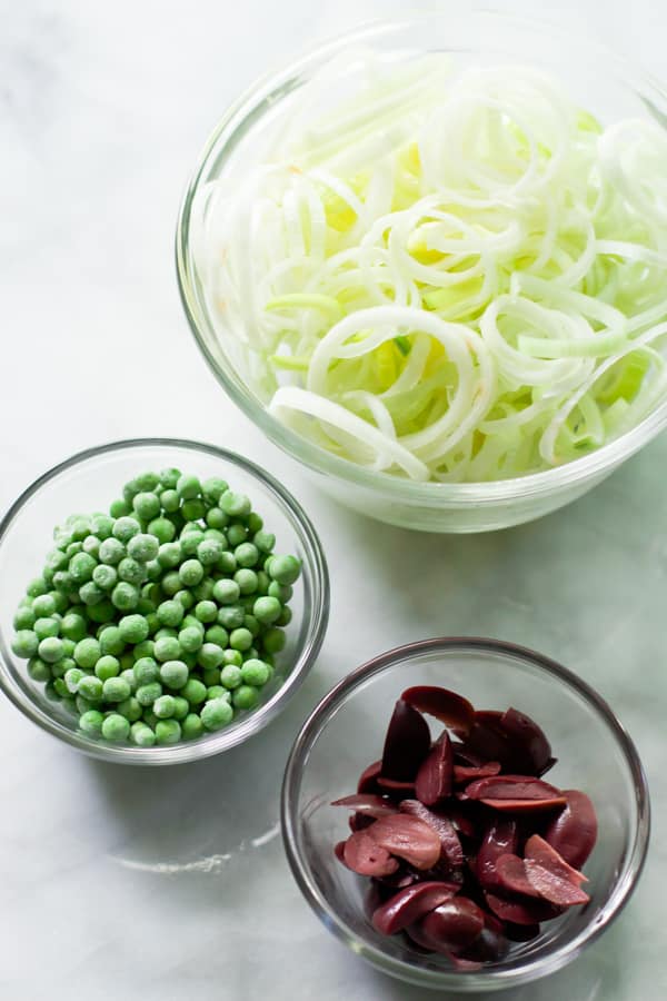 Prep bowls with sliced leeks, frozen peas, and kalamata.