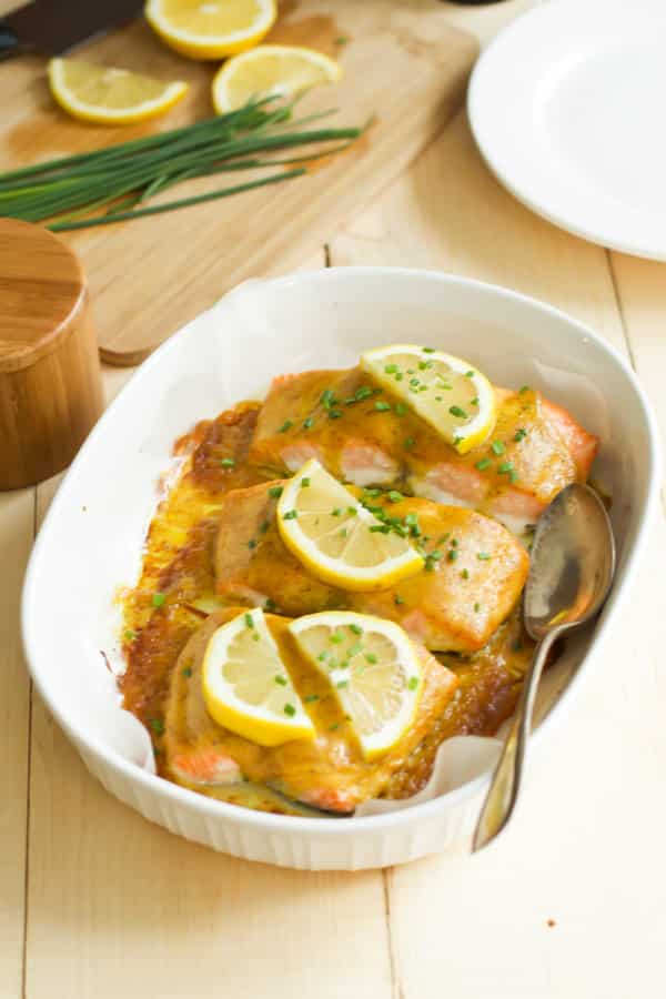 Maple mustard salmon in a baking dish with a spoon inside.