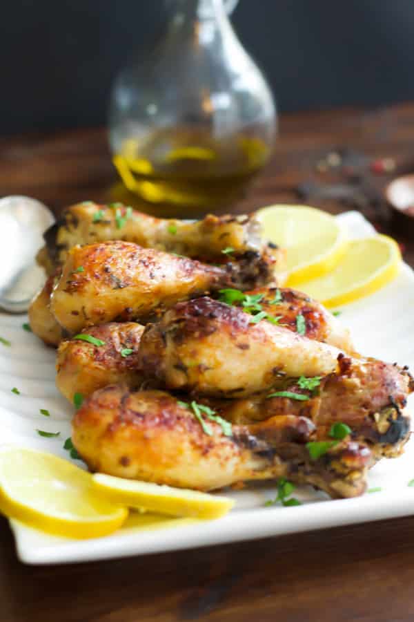 Roasted Lemon Chicken Legs arranged on a white serving plate garnished with lemon wedges.