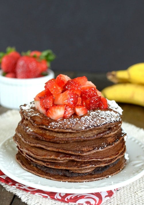 Skinny-Chocolate-Banana-Oatmeal-Pancakes-1 A stack of skinny chocolate banana oatmeal pancakes with strawberries and powdered sugar on top.