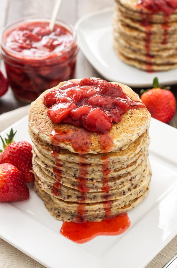 A stack of strawberry quinoa pancakes with strawberry sauce drizzling down.