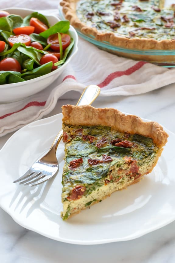 A slice of pesto quiche with sun-dried tomatoes and parmesan.