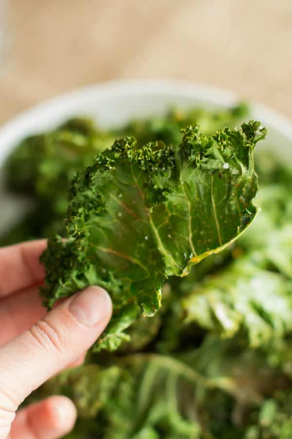 Spicy kale chips in a bowl with one being held in focus.