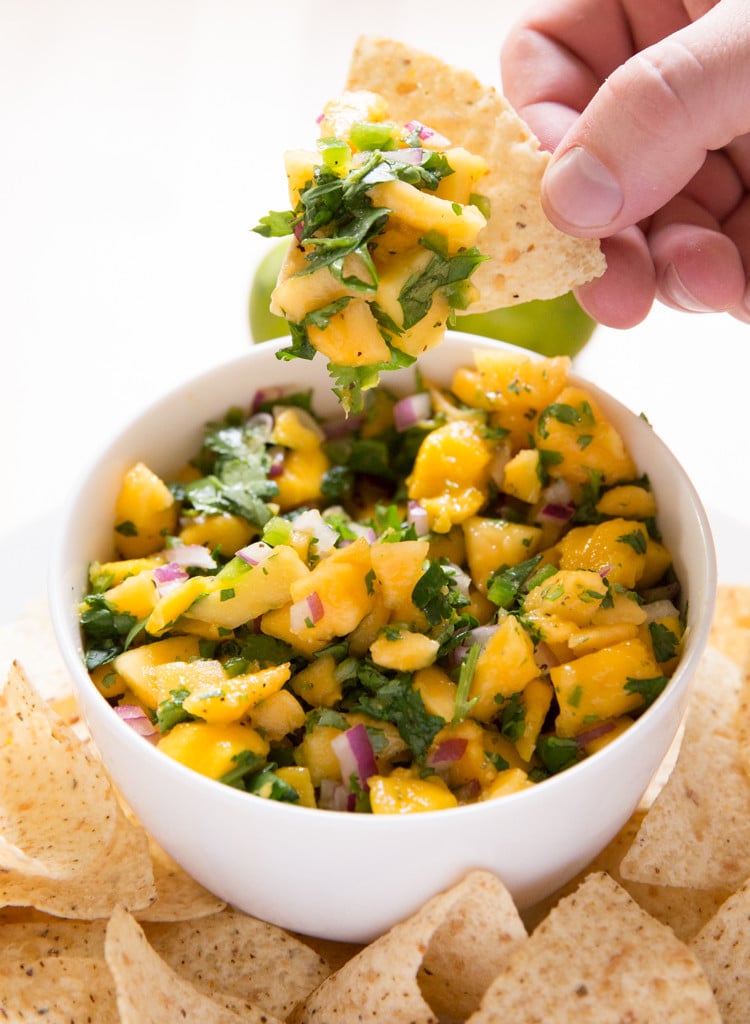 Tropical mango papaya fruit salsa in a bowl with a tortilla chip scooping some out.