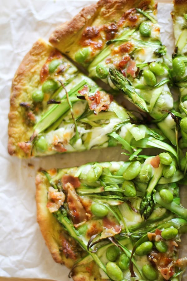 A close up of a cut slice of asparagus and pancetta pesto pizza.