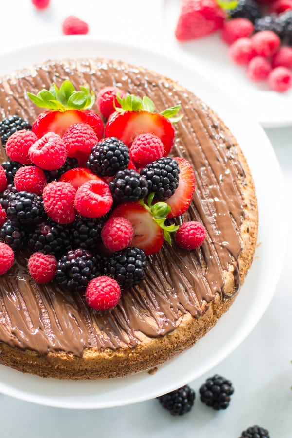 An overhead image of an almond cake with berries on a cake stand.