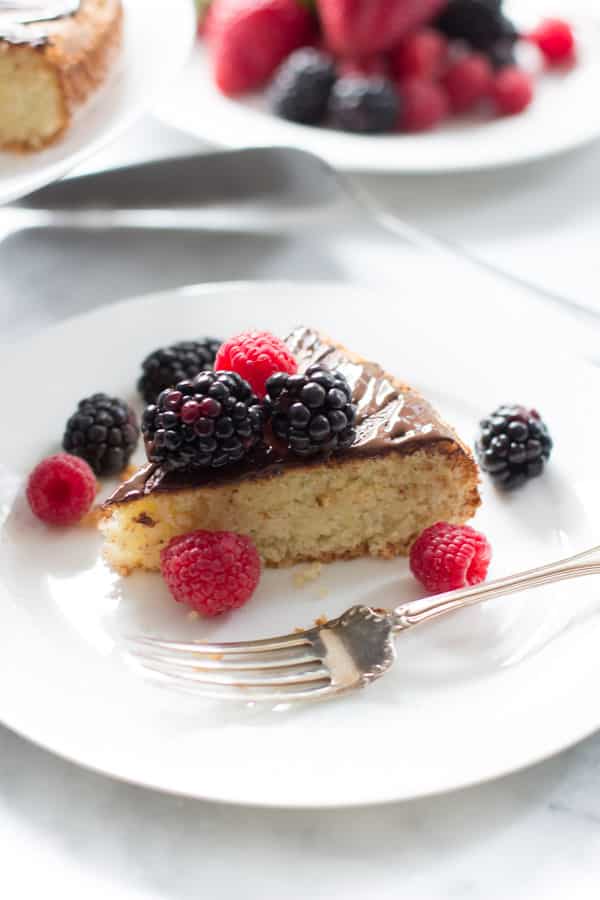 A slice of almond cake with berries on a plate with a fork.