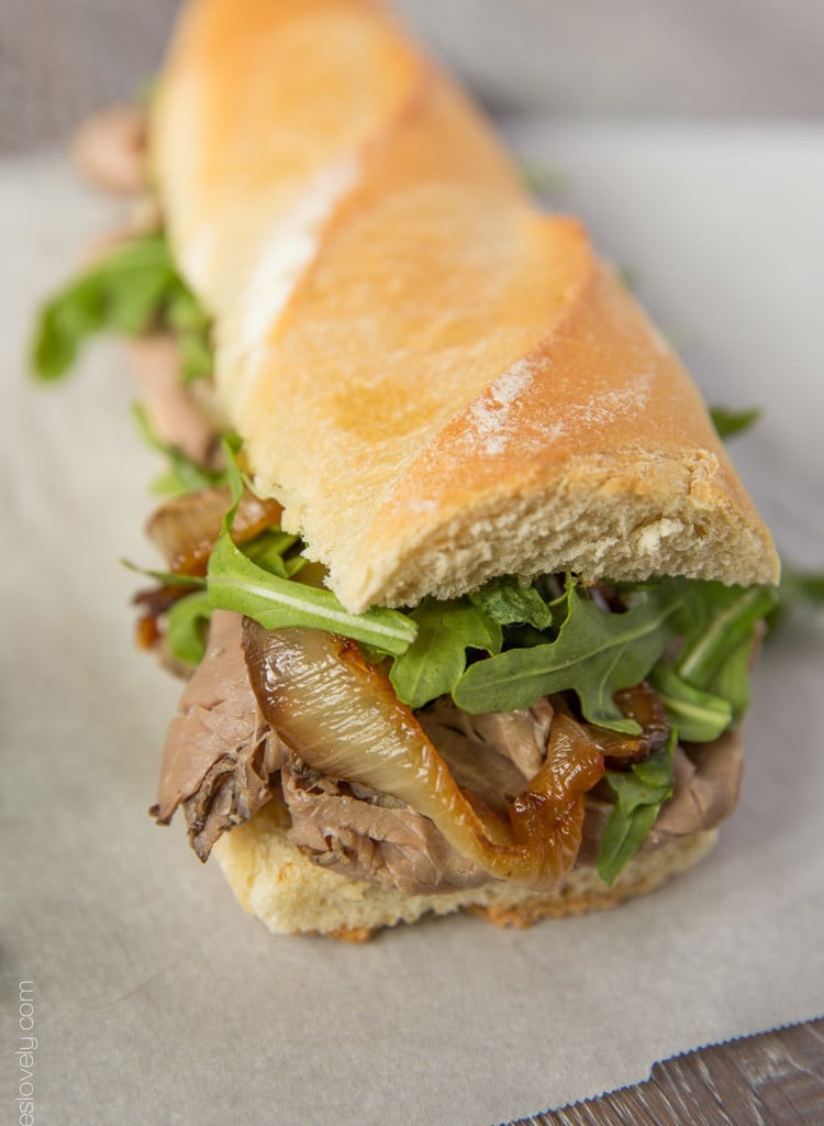 A side view of a Beef Dip Sandwich with Gruyere & Grilled Onions on parchment paper.