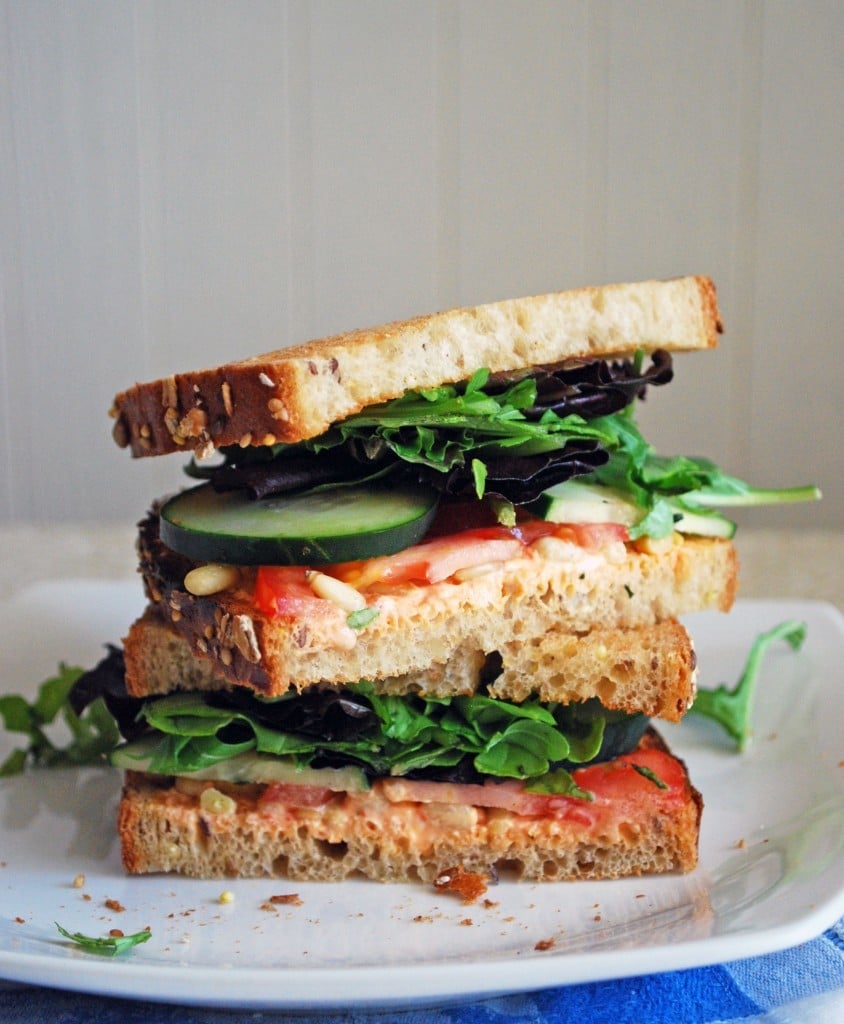 Two halves of a Goat Cheese and Veggie Sandwich stacked on top of each other on a white plate.