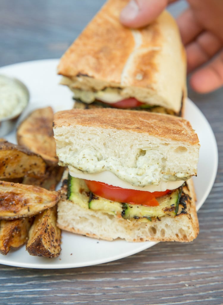 A Grilled Zucchini Caprese Sandwich on a white plate with a side of potato wedges.