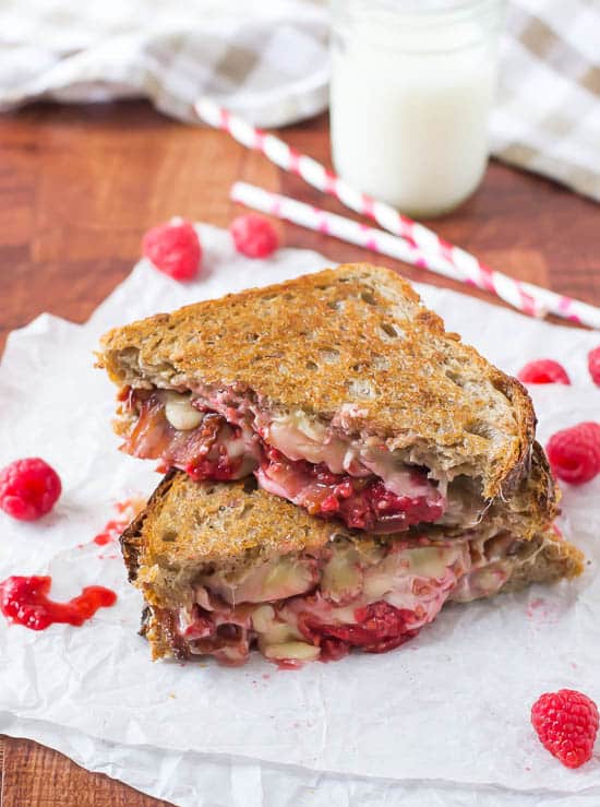 Two halves of a Raspberry Chipotle Bacon Grilled Cheese stacked on parchment paper.