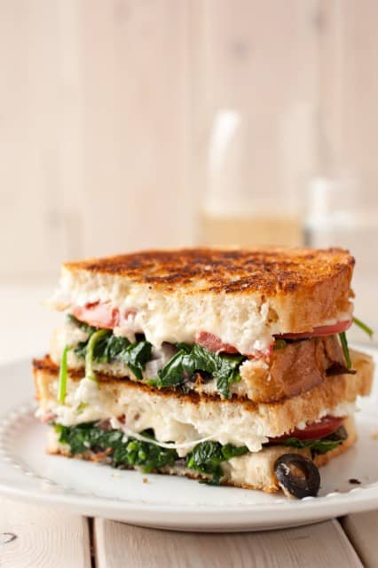 mediterranean-grilled-cheese-sandwich Two halves of a Mediterranean Grilled Cheese Sandwich stacked on a white plate.